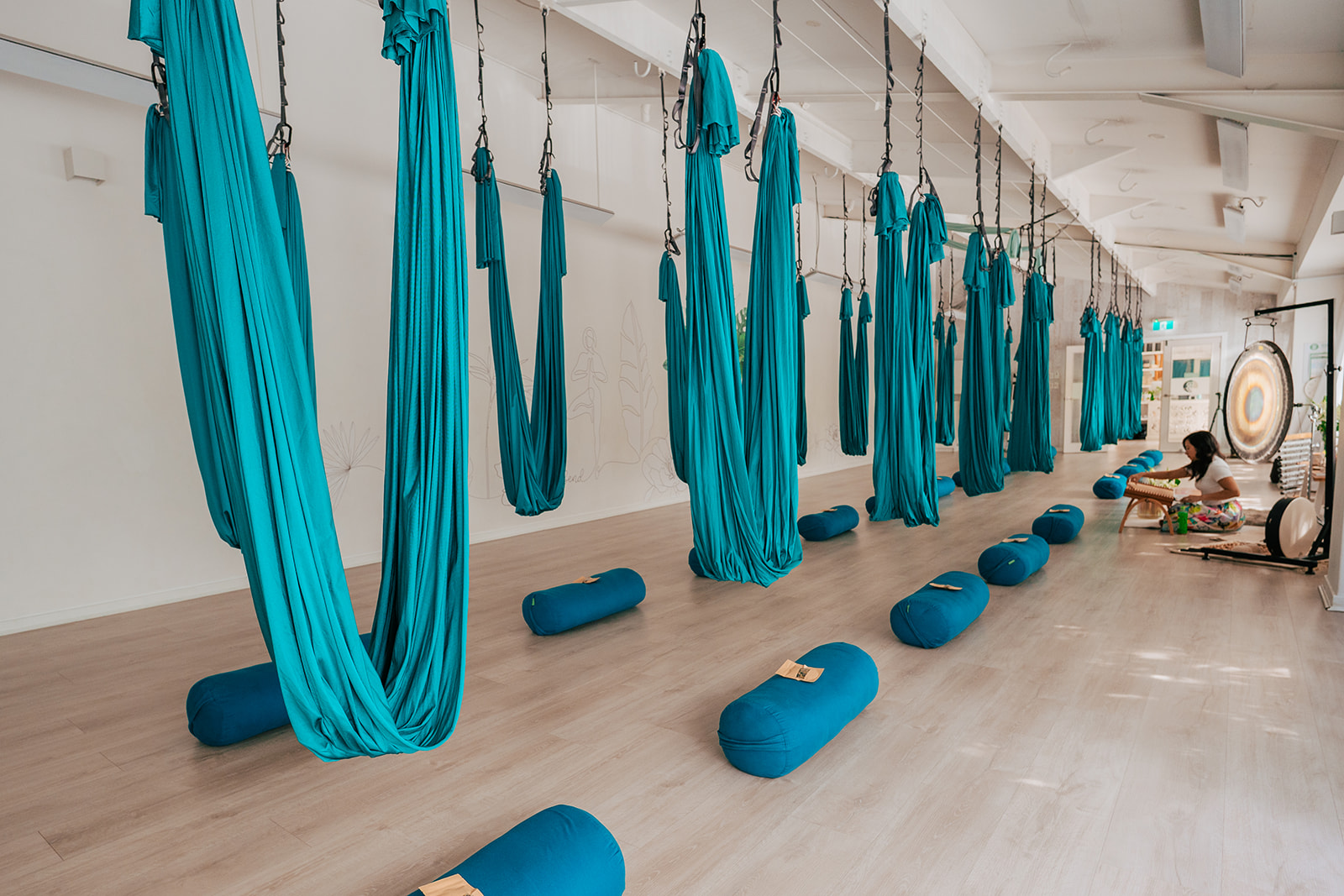Participants floating in aerial yoga hammocks during a sound bath meditation, surrounded by soothing sounds from crystal singing bowls, gongs, and chimes, creating a deep sense of relaxation and inner stillness.